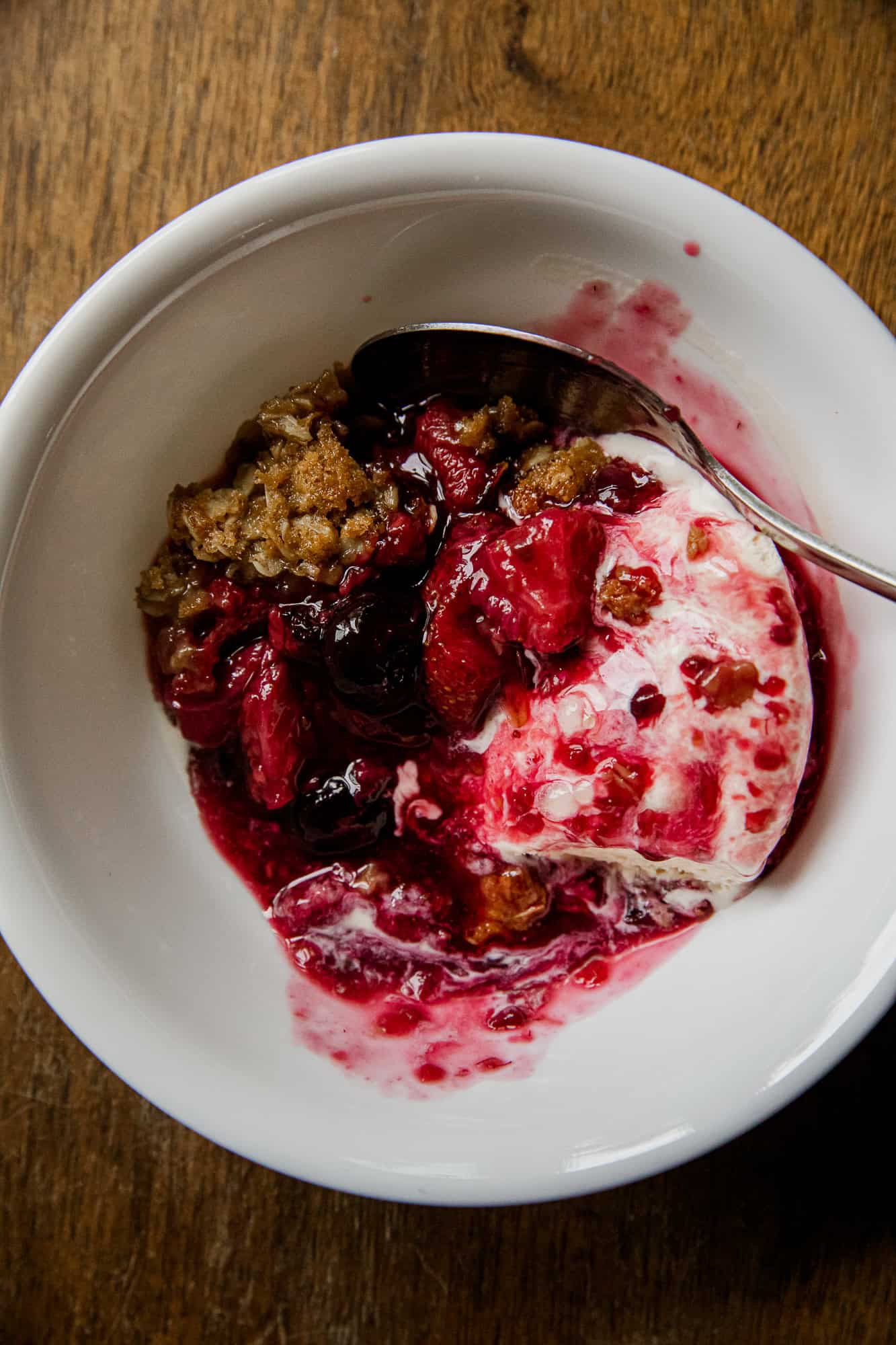 Berry crisp with mixed berries and crumble topping in white bowl.