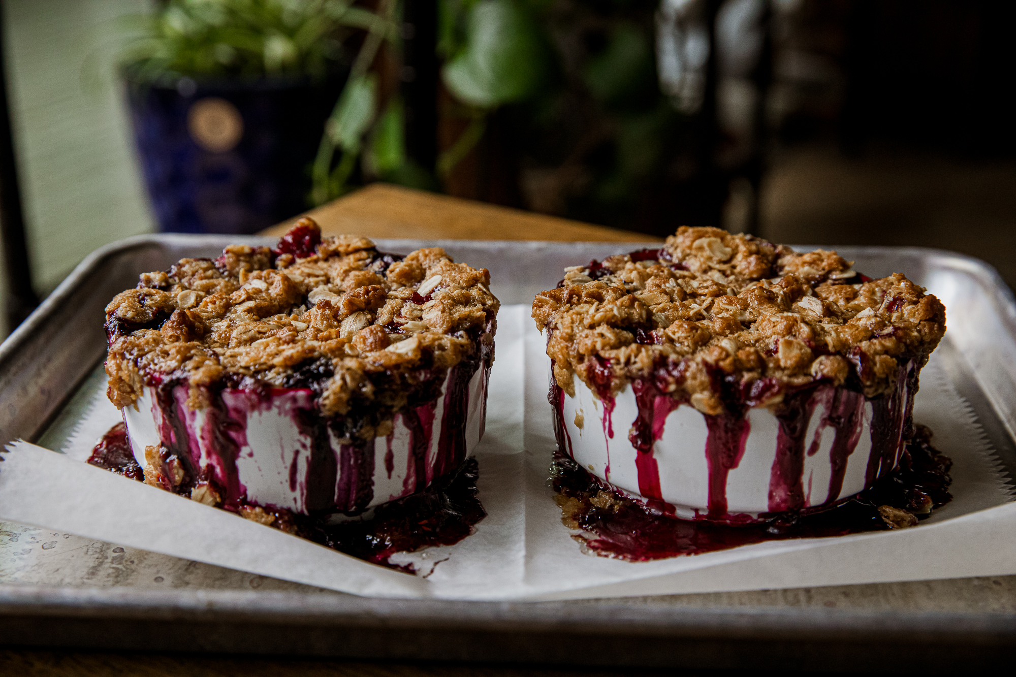Two berry crisp desserts with drizzled berry sauce on a baking sheet.