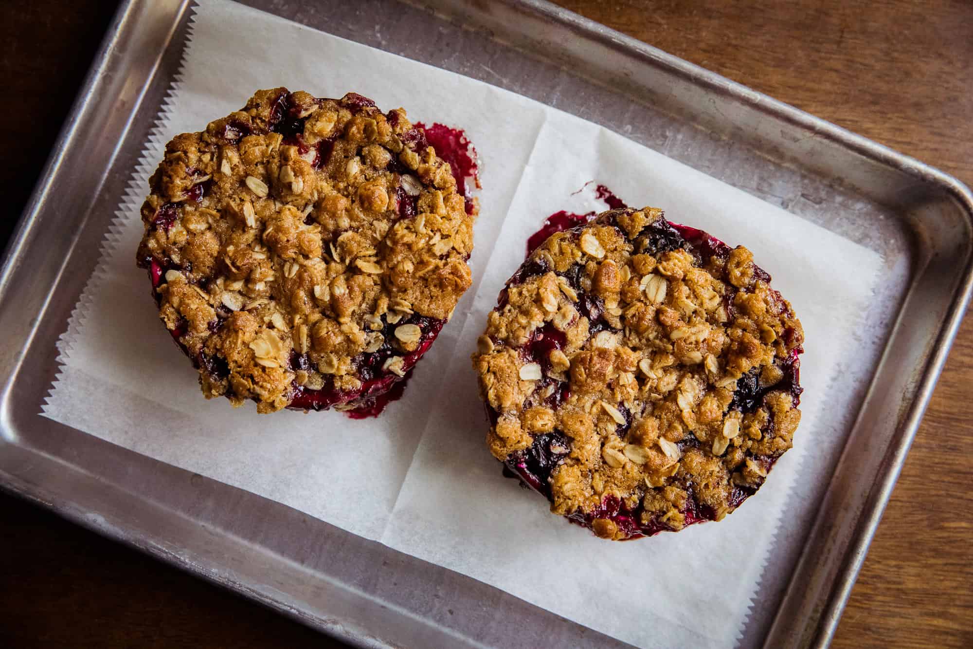 Two berry crisp muffins on a baking sheet with parchment paper.