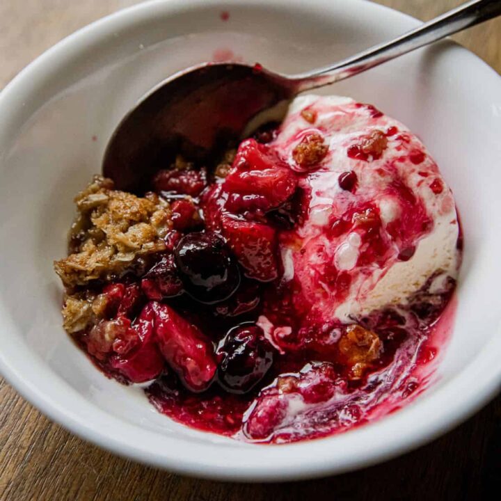 Close-up of berry crisp with ice cream in a white bowl.