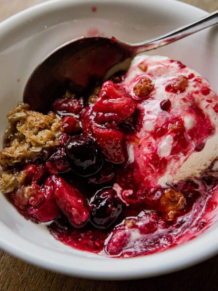 Close-up of berry crisp with ice cream in a white bowl.