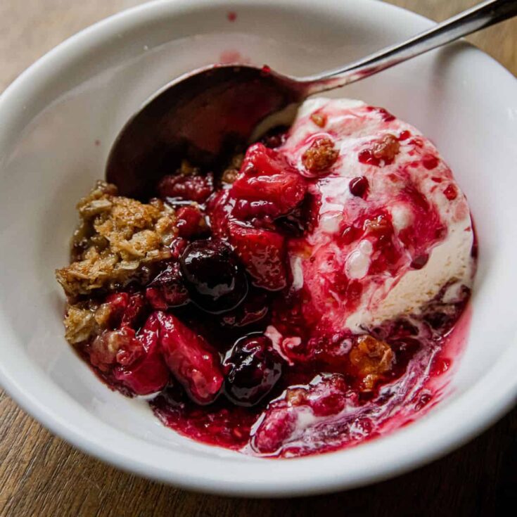 Close-up of berry crisp with ice cream in a white bowl.