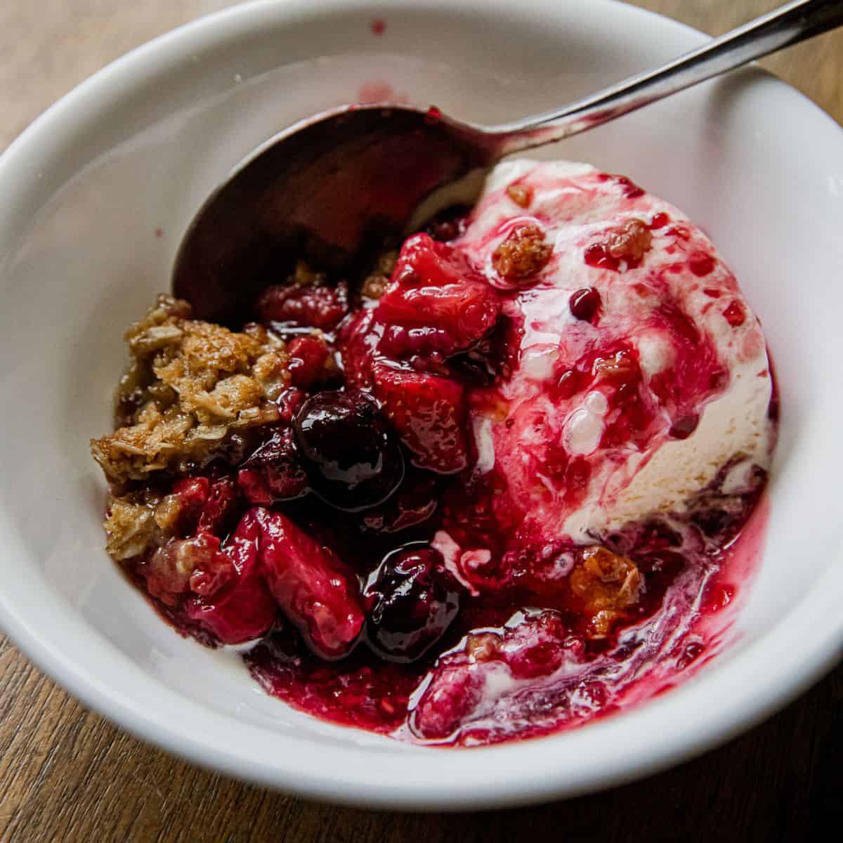 Close-up of berry crisp with ice cream in a white bowl.