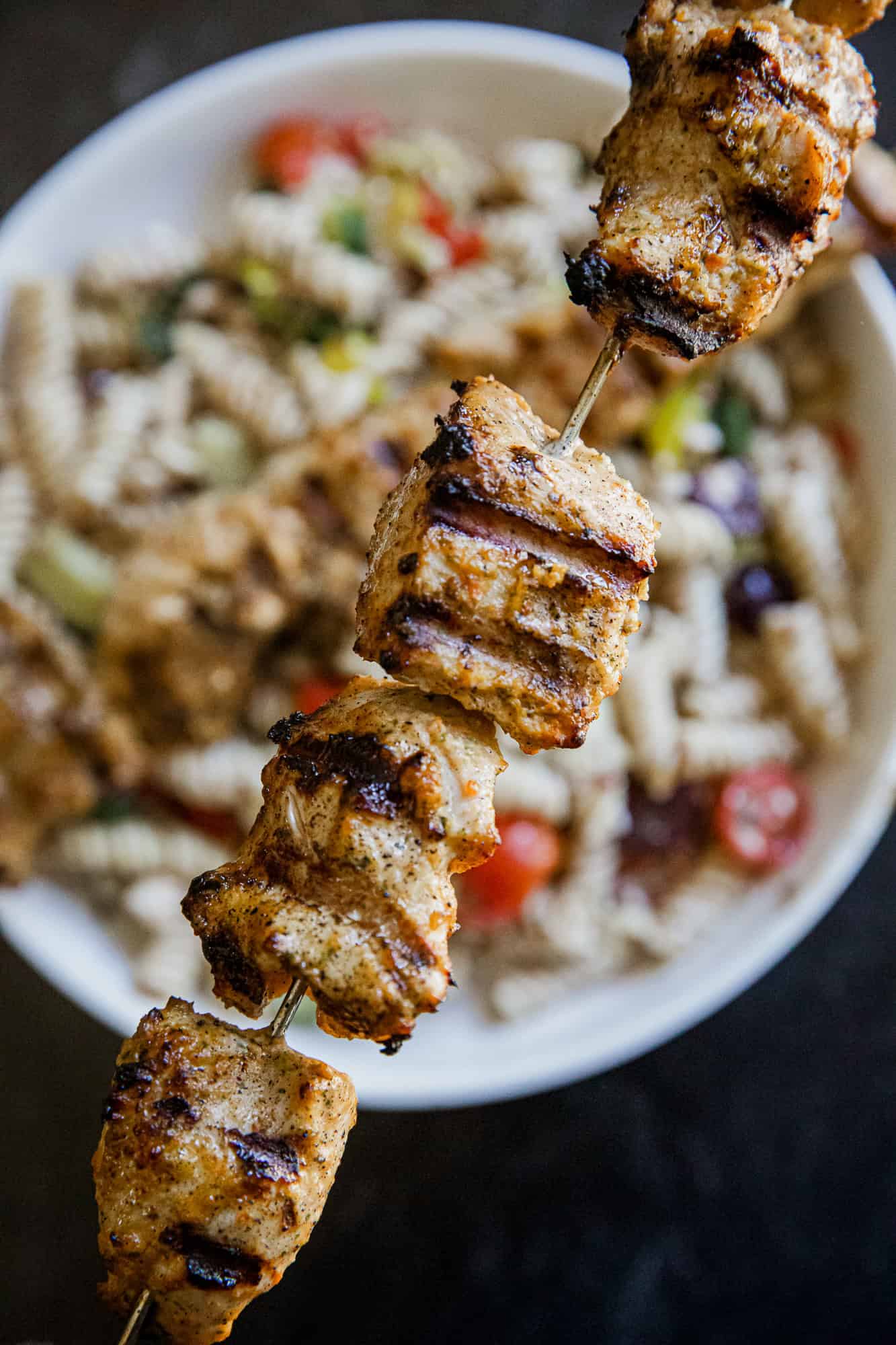 Close-up of grilled jerk chicken kabobs on a skewer with rice salad in background.