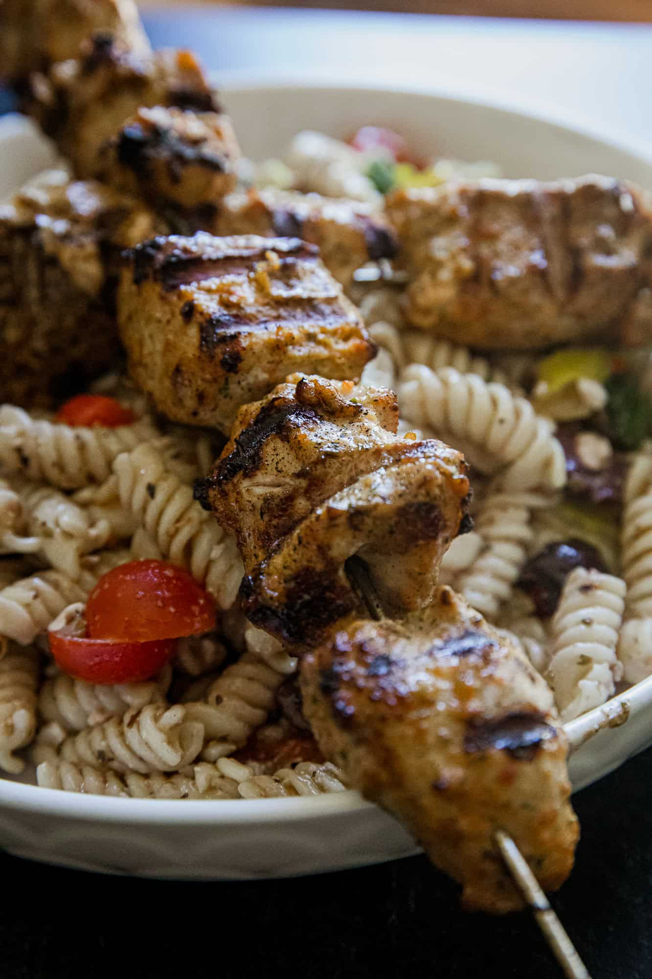 Juicy grilled jerk chicken skewers served over pasta salad with vegetables.