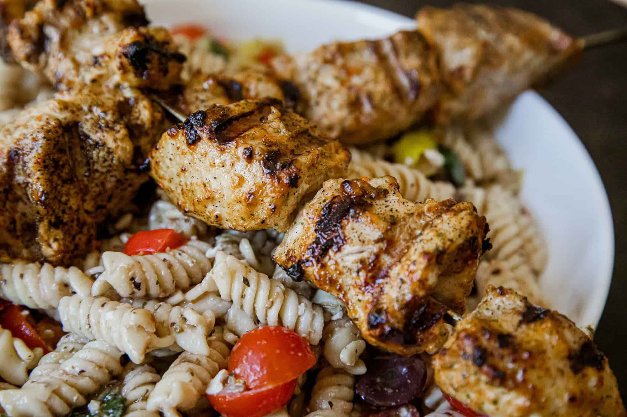 Juicy grilled chicken skewers served over pasta salad with vegetables.
