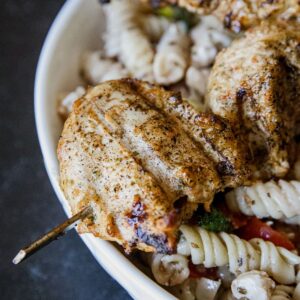 Juicy grilled chicken served with pasta and fresh vegetables in a white bowl.