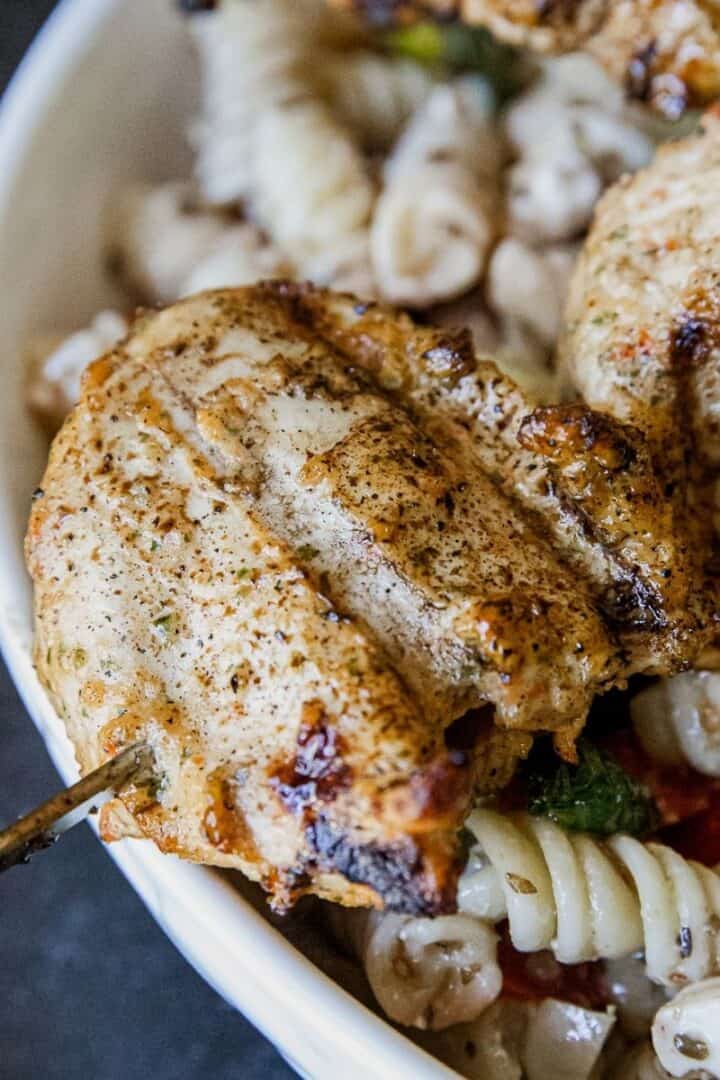 Juicy grilled chicken served with pasta and fresh vegetables in a white bowl.