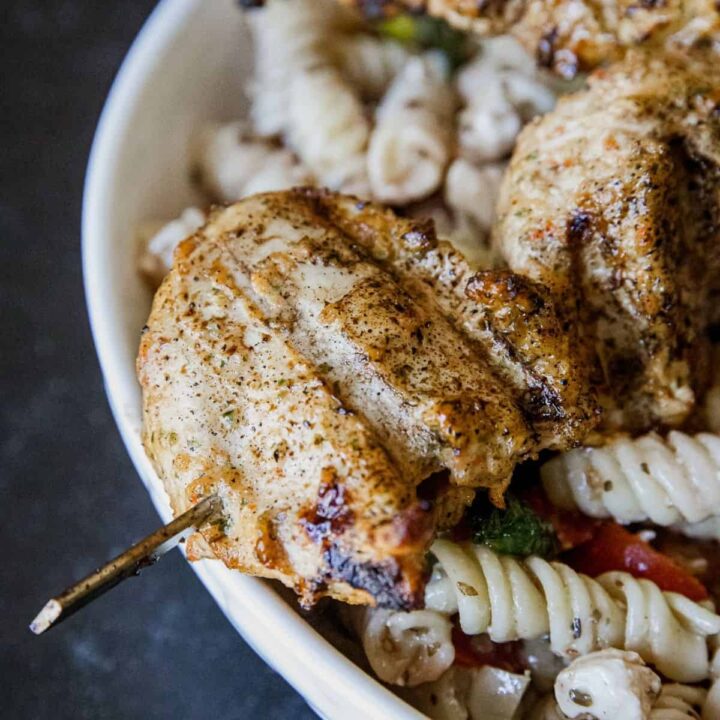 Juicy grilled chicken served with pasta and fresh vegetables in a white bowl.