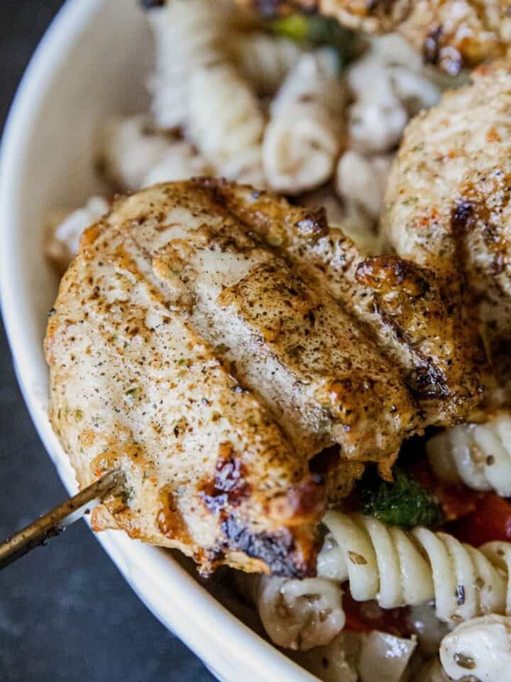 Juicy grilled chicken served with pasta and fresh vegetables in a white bowl.
