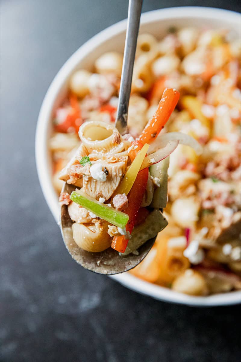 Close-up of pasta salad with grilled chicken, vegetables, and balsamic dressing.