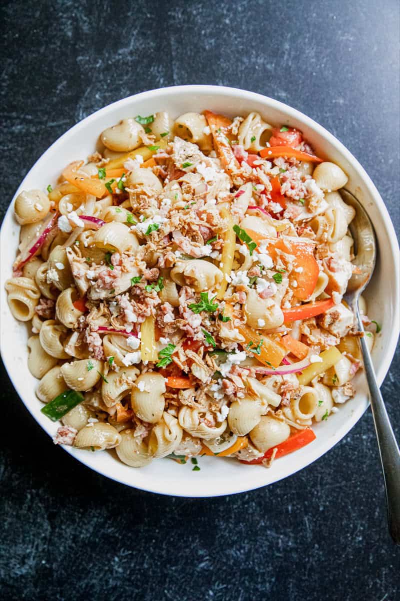 Colorful pasta salad with grilled chicken, vegetables, and cheese in a white bowl.