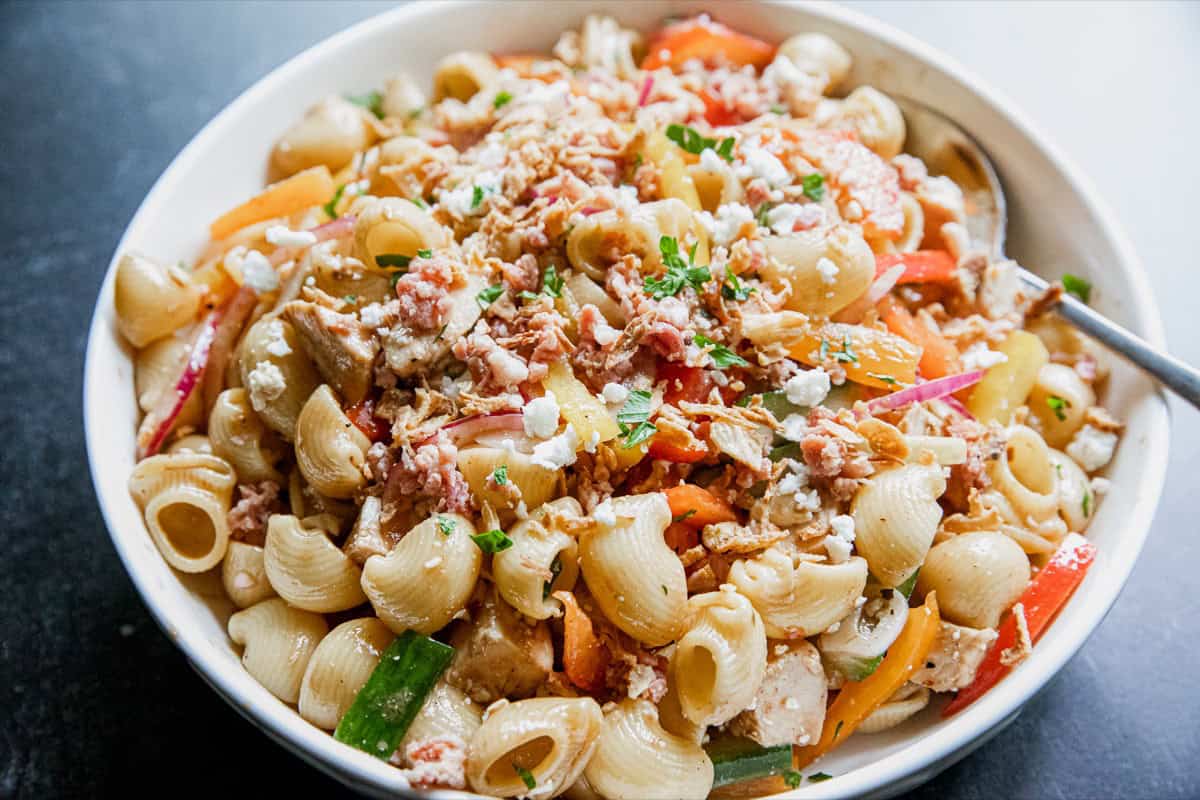 Close-up of pasta salad with chicken, vegetables, and cheese in a white bowl.