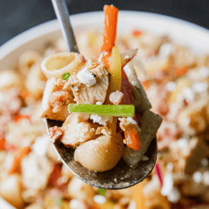 Close-up of pasta salad with chicken, vegetables, and balsamic dressing on a spoon.