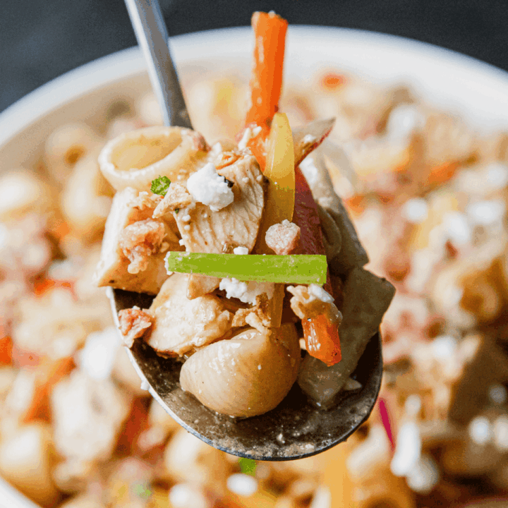 Close-up of pasta salad with chicken, vegetables, and balsamic dressing on a spoon.