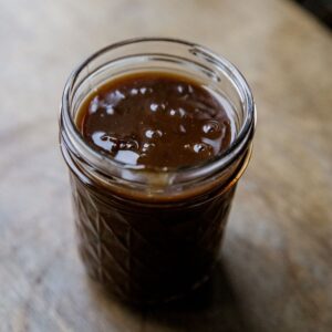 Close-up of beef protein gravy in a glass jar on a wooden surface.
