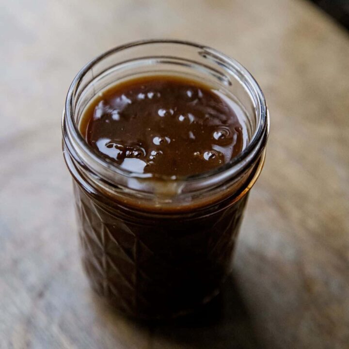 Close-up of beef protein gravy in a glass jar on a wooden surface.