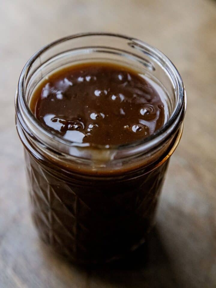 Close-up of beef protein gravy in a glass jar on a wooden surface.