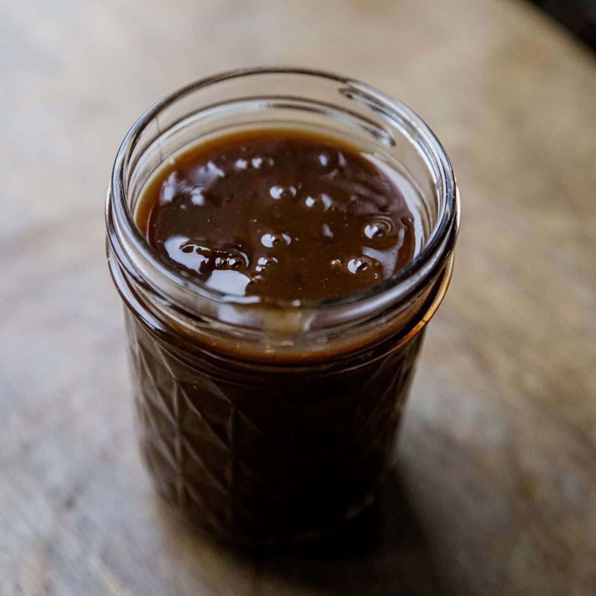 Close-up of beef protein gravy in a glass jar on a wooden surface.