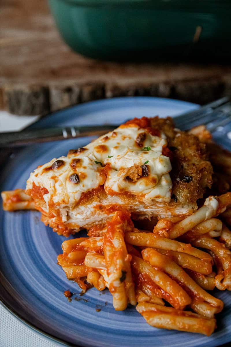 Close-up of Chicken Parmesan with pasta on a blue plate.