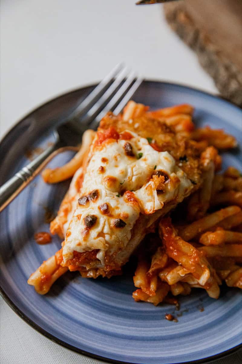 Close-up of Chicken Parmesan served with pasta on a blue plate.