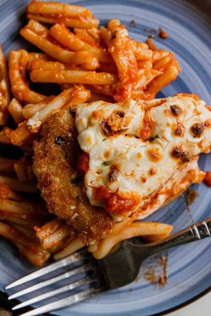 Chicken Parmesan served with spaghetti and marinara sauce on a blue plate.