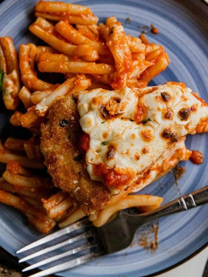 Chicken Parmesan served with spaghetti and marinara sauce on a blue plate.