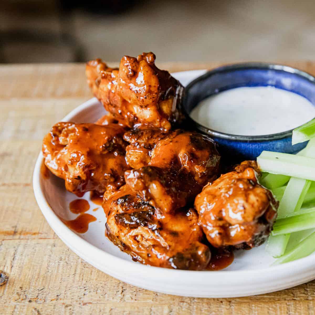 Juicy BBQ chicken wings with celery and dipping sauce on a white plate.