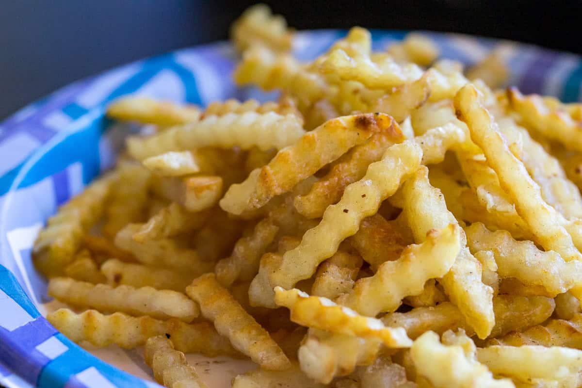 Golden crispy French fries served in a blue and white paper basket.