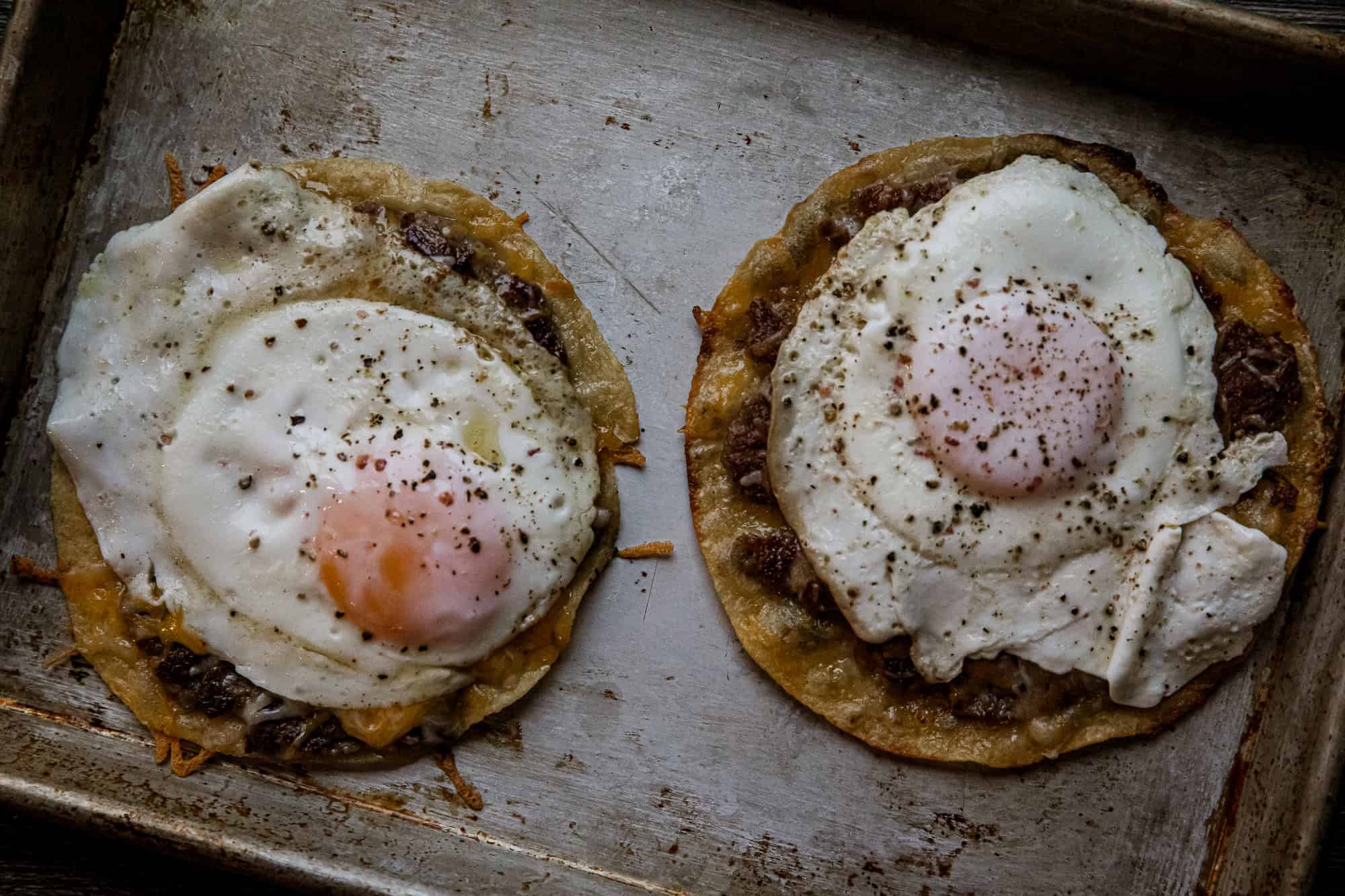 Two breakfast tacos with fried eggs on top, served on a rustic tray.