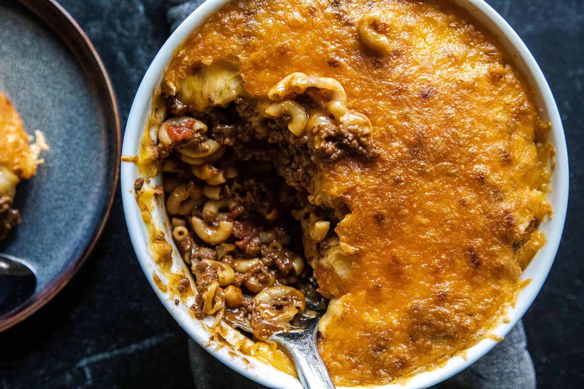 Baked chili mac casserole with cheese and pasta in a white dish.