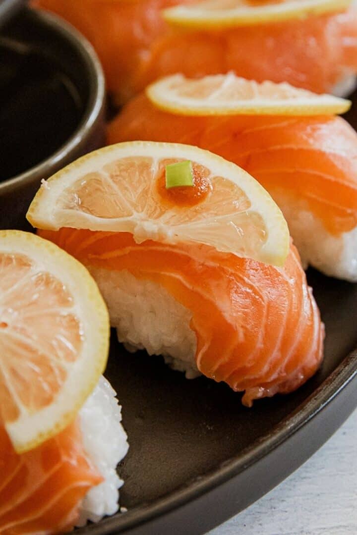 Salmon nigiri sushi with lemon slices on top, served with soy sauce.