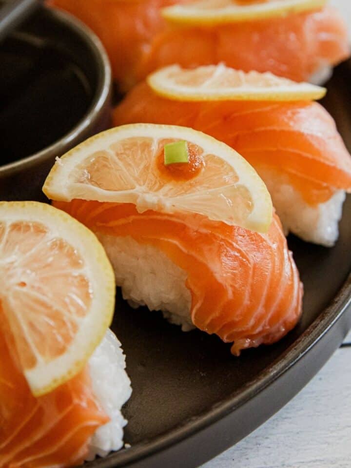 Salmon nigiri sushi with lemon slices on top, served with soy sauce.