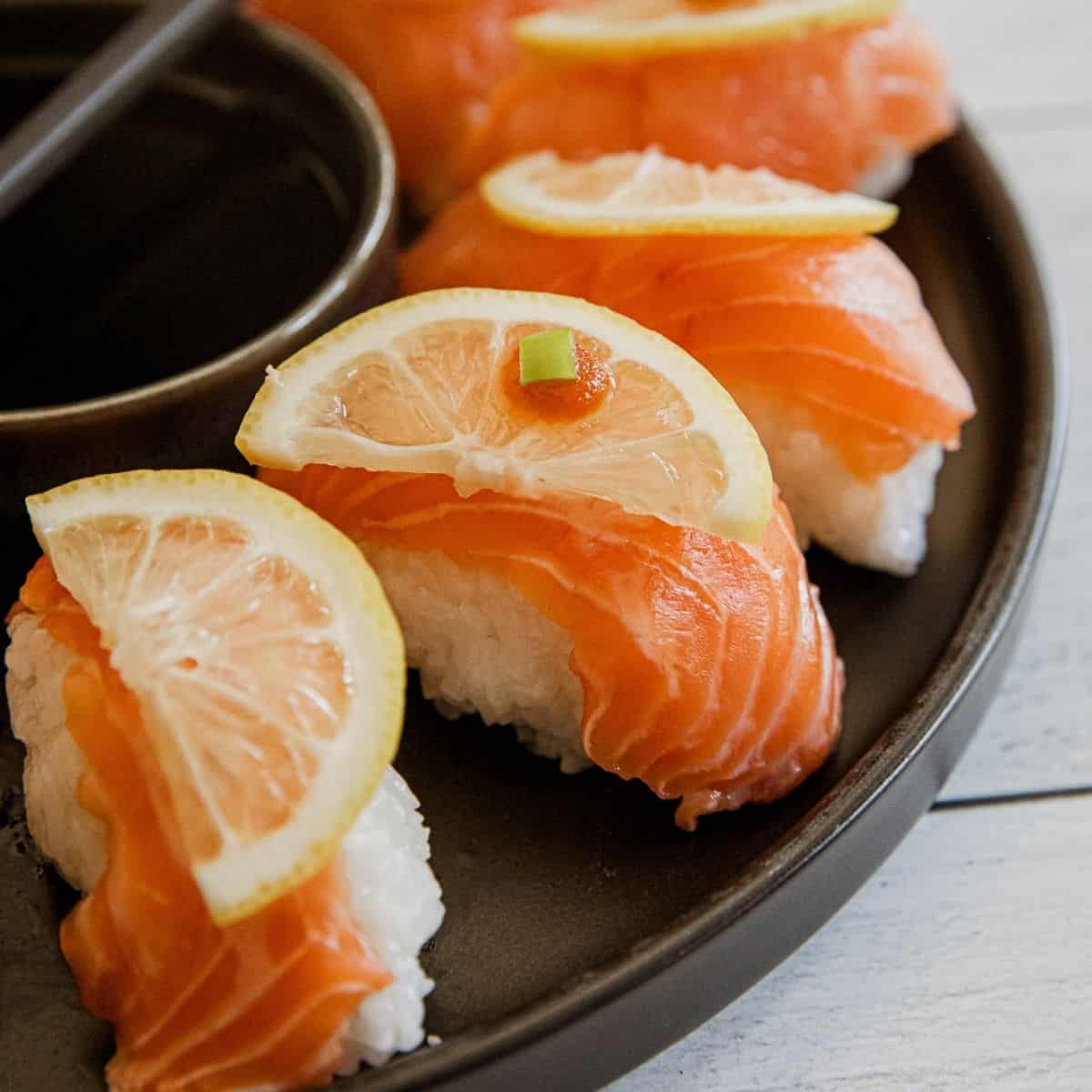 Salmon nigiri sushi with lemon slices on top, served with soy sauce.