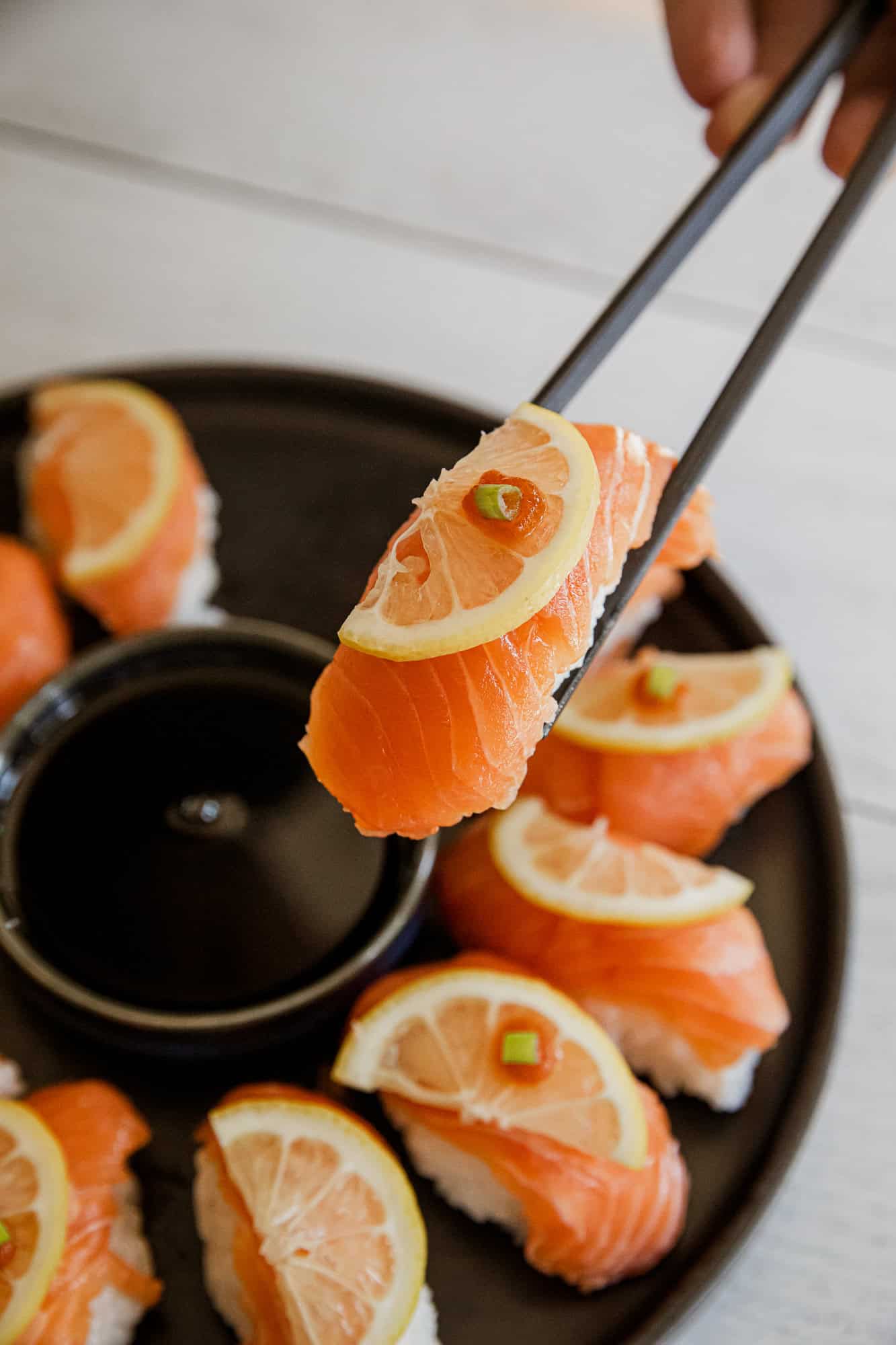 Fresh salmon nigiri with lemon slice and green onion topping.