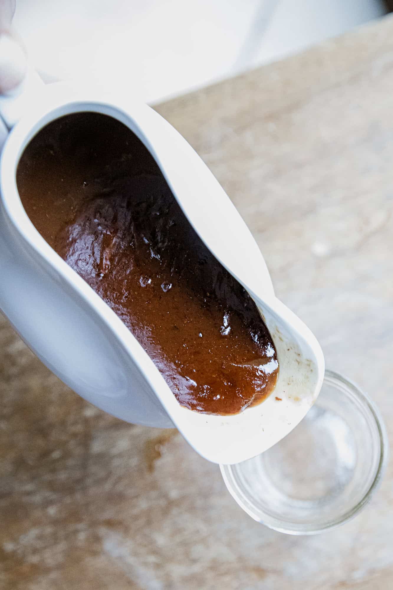 Rich beef protein gravy being poured from a white gravy boat into a glass bowl.