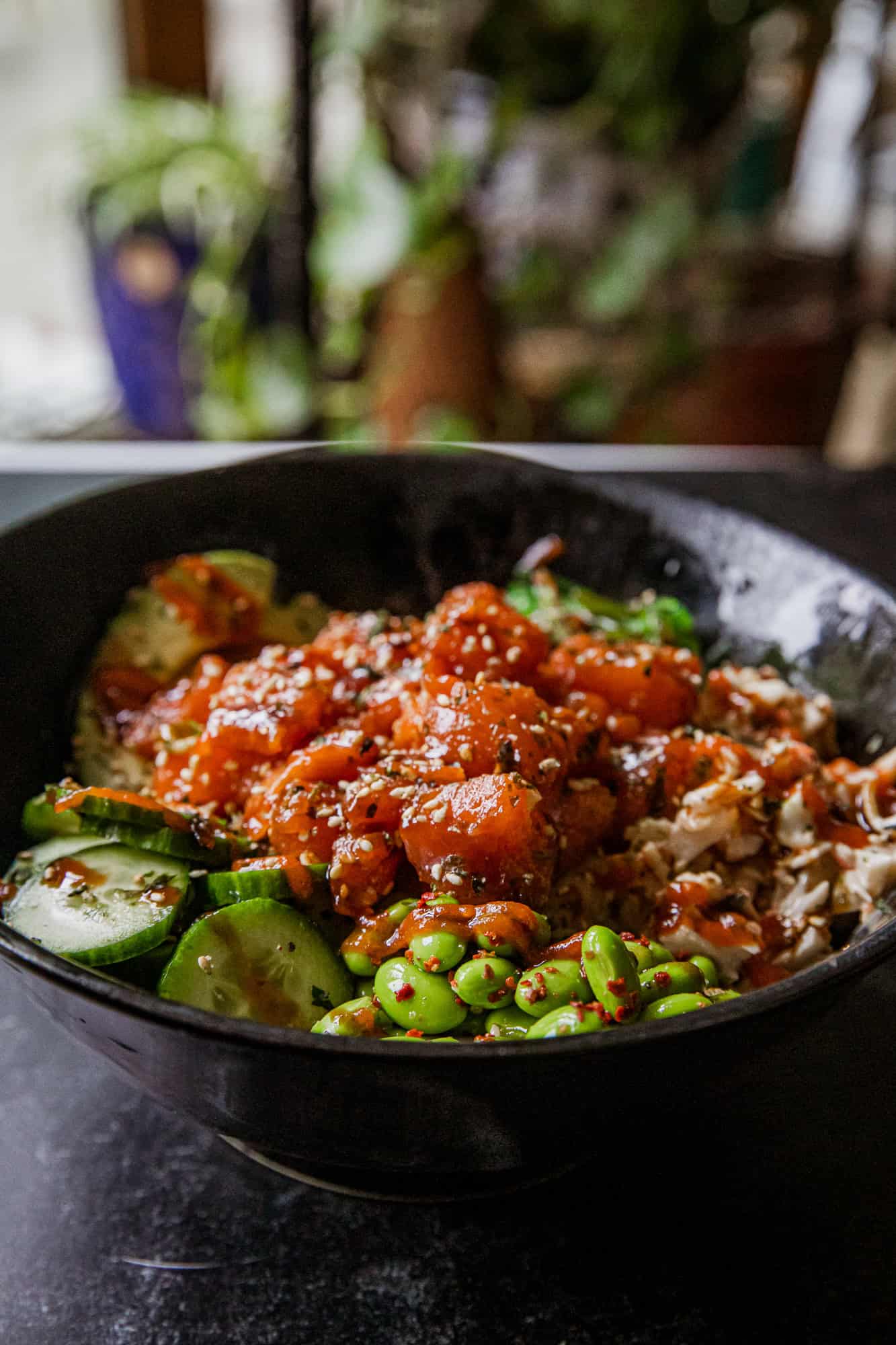Close-up of spicy salmon poke bowl with vegetables and rice in black bowl.
