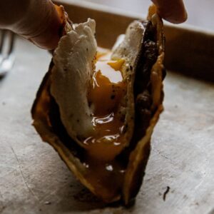 Close-up of a breakfast taco with egg and meat filling, held by hand.