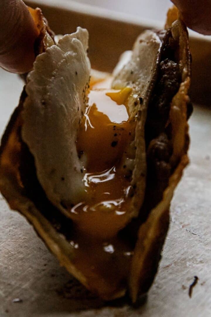 Close-up of a breakfast taco with egg and meat filling, held by hand.