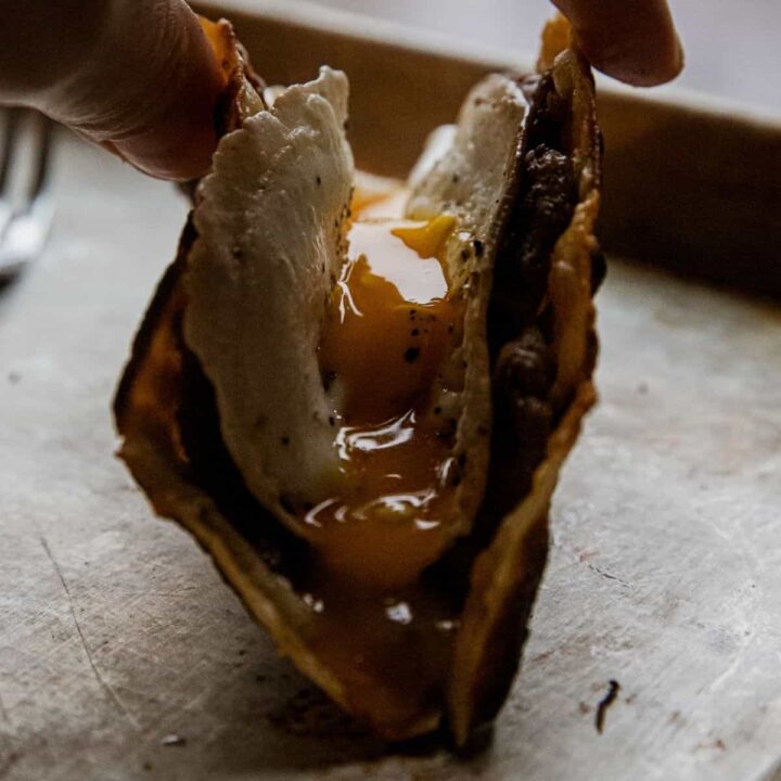 Close-up of a breakfast taco with egg and meat filling, held by hand.