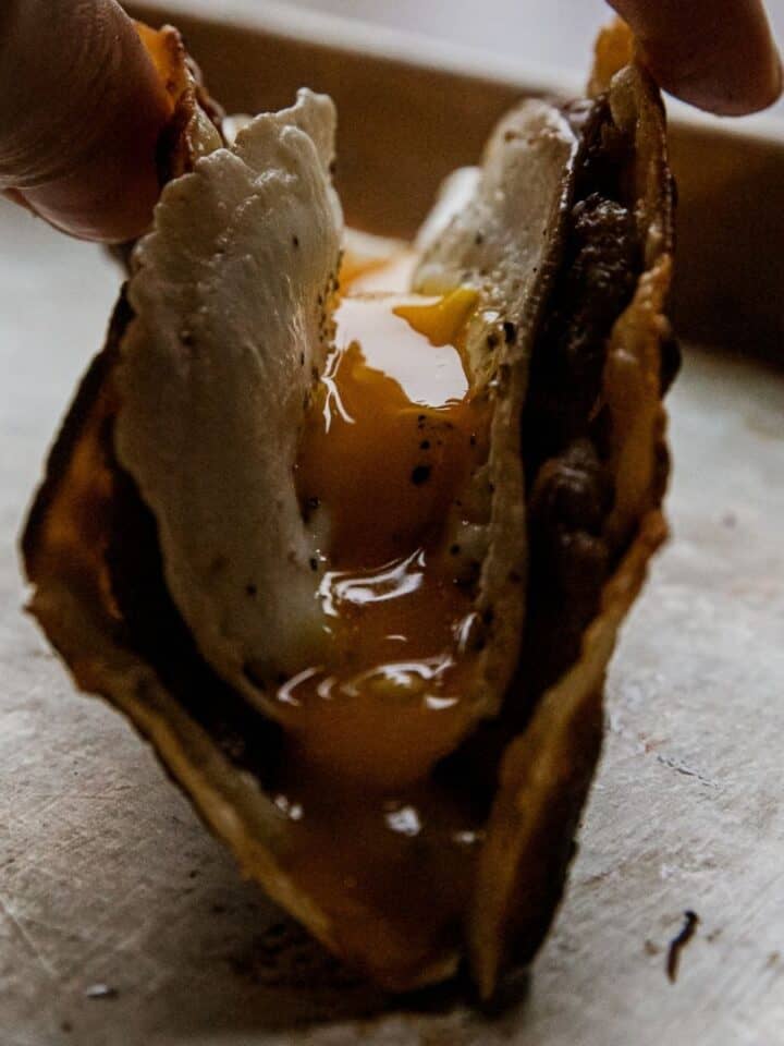 Close-up of a breakfast taco with egg and meat filling, held by hand.