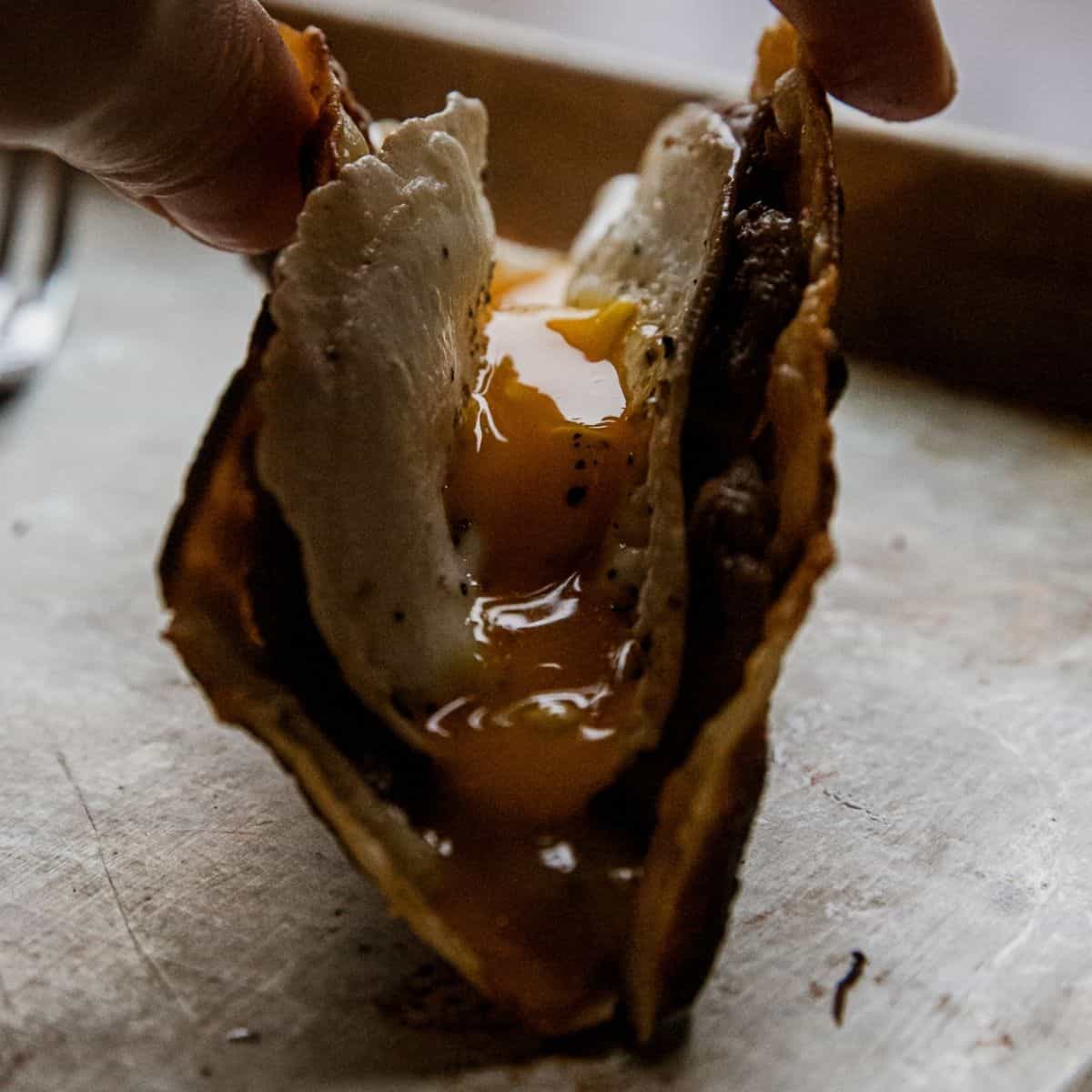 Close-up of a breakfast taco with egg and meat filling, held by hand.