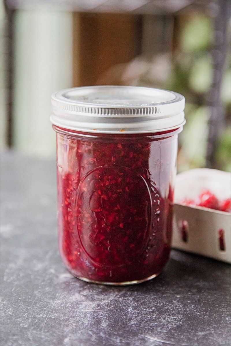 Glass jar filled with homemade tayberry jam on a kitchen countertop.
