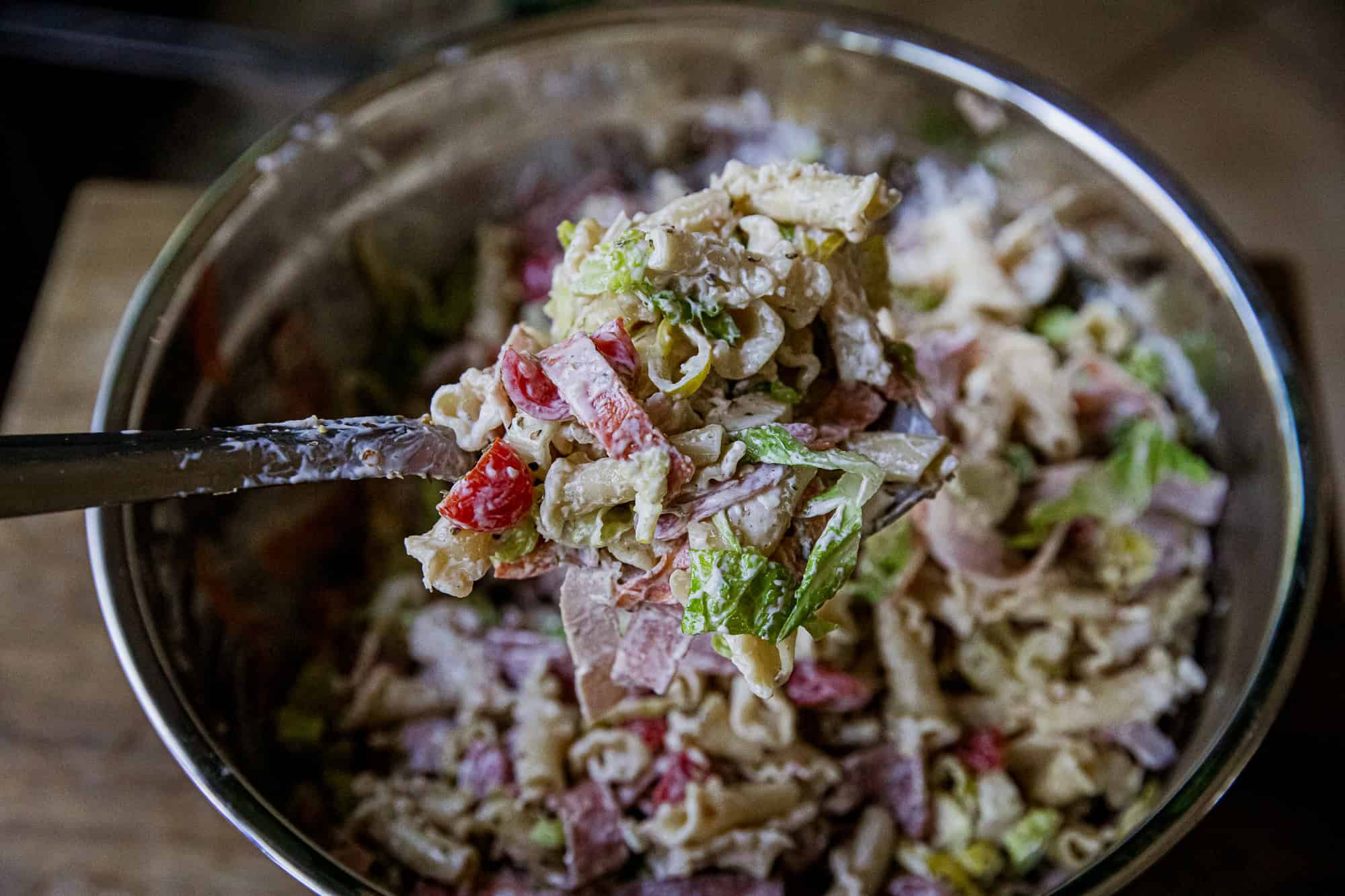 Close-up of Italian grinder pasta salad with vegetables and cheese in a glass bowl.