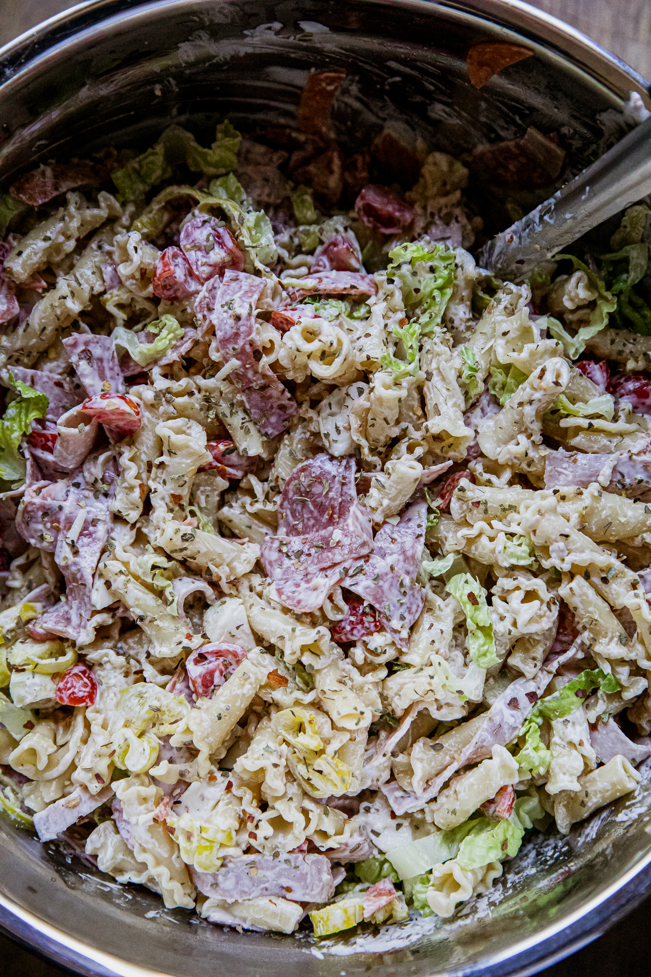 Creamy pasta salad with ham, lettuce, and cherry tomatoes in a metal bowl.
