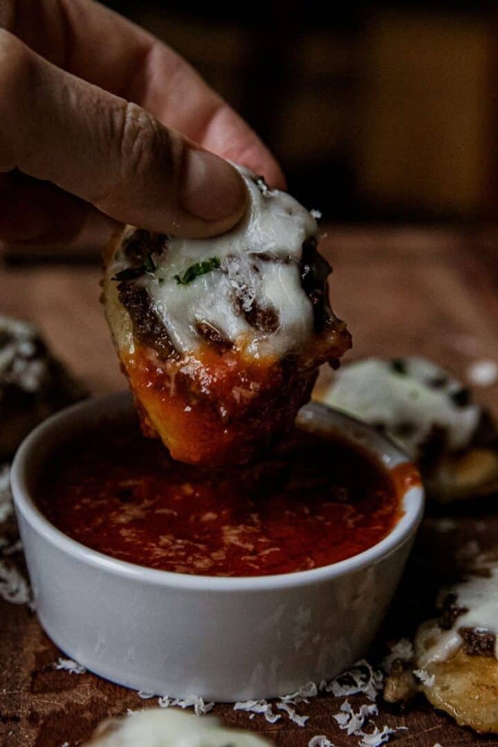 Mini meatball sub bites dipped in marinara sauce with melted cheese.