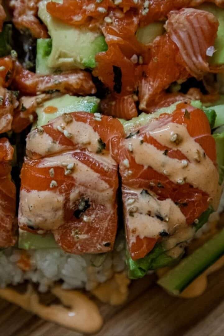 Close-up of salmon sushi stack with avocado and spicy mayo.