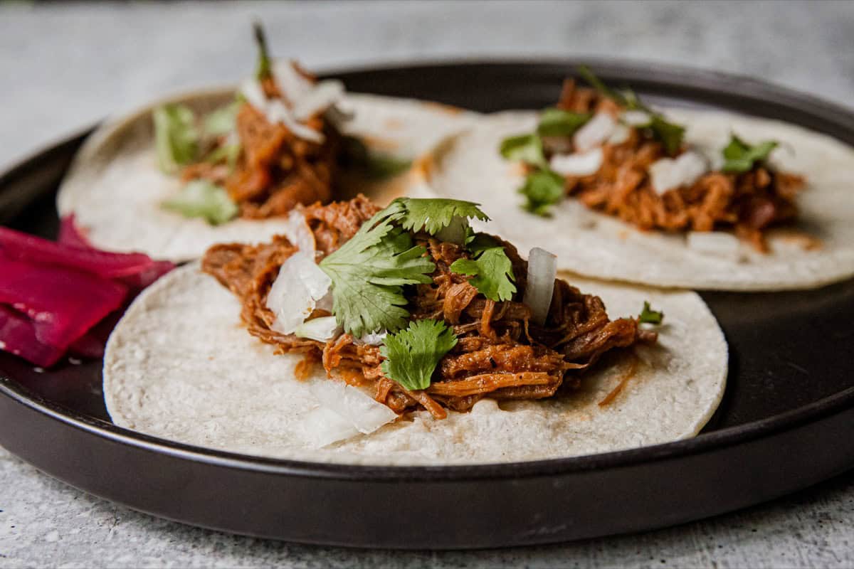 Delicious venison barbacoa tacos with cilantro and onions on a black plate.