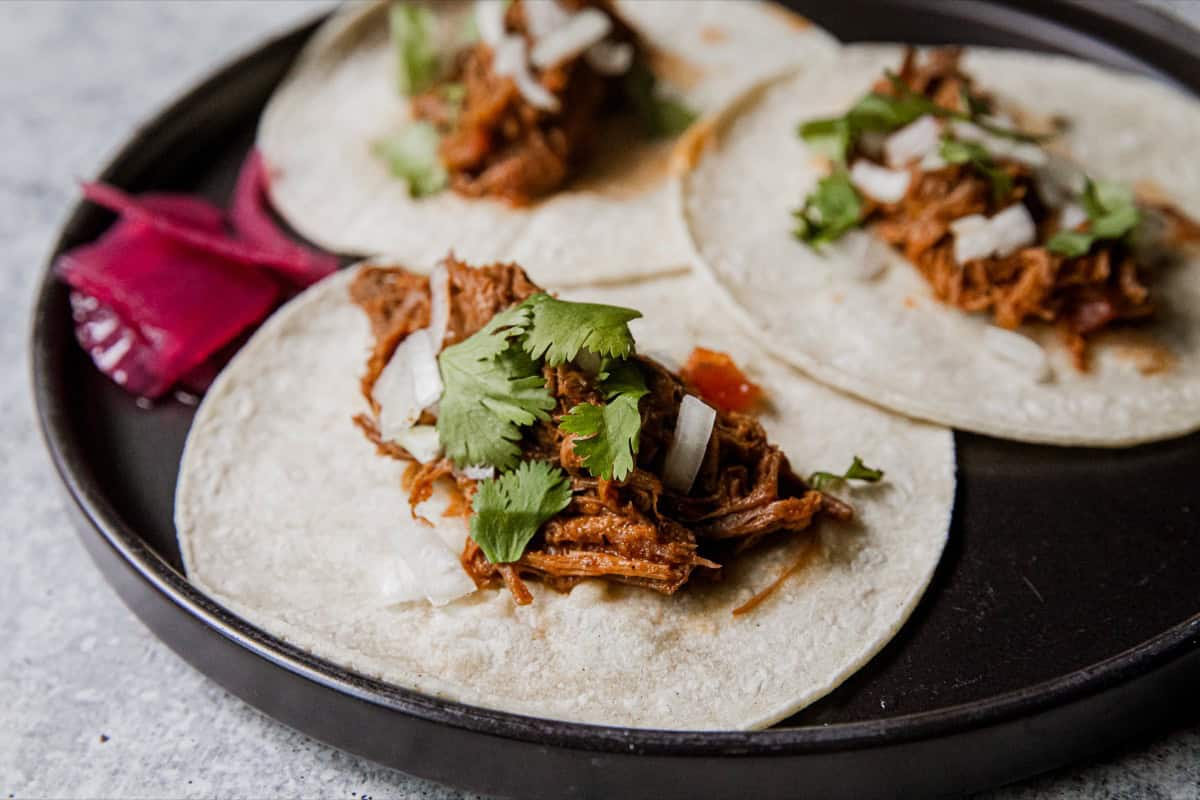 Delicious venison barbacoa tacos with cilantro and onions on a black plate.