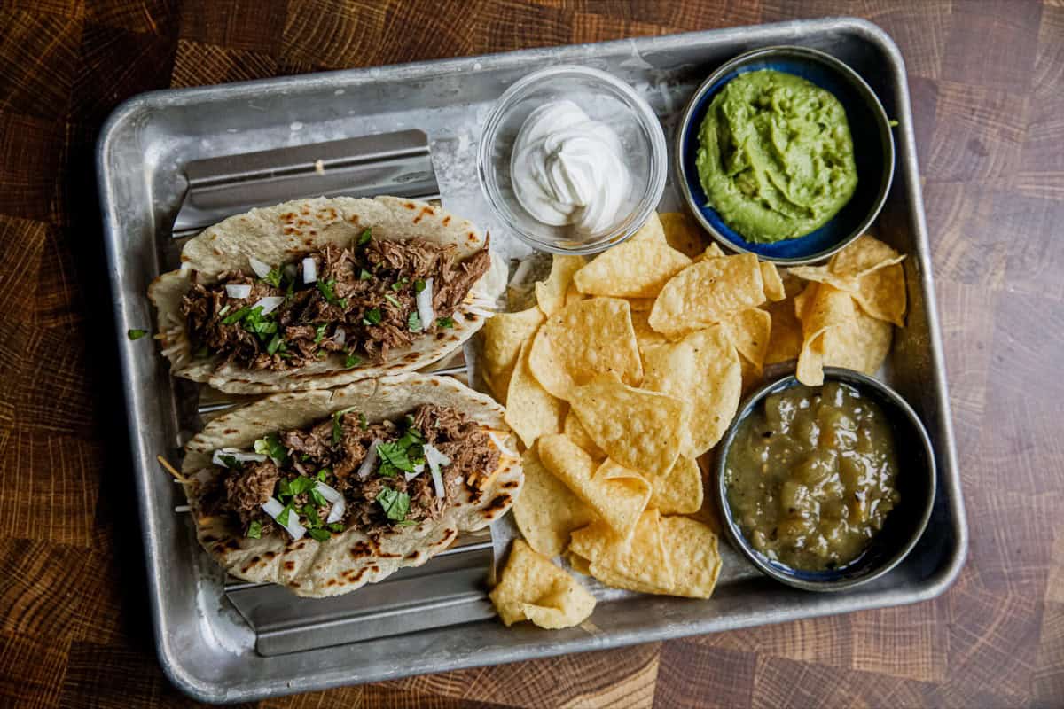 Chuck roast tacos on a platter with chips, salsa, and guacamole.